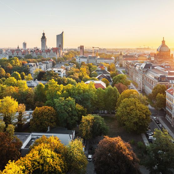 Skyline von Leipzigs Innenstadt bei Sonnenaufgang im Spätsommer, am Horizont sieht man wichtige Sehenswürdigkeiten aus Leipzig wie das City-Hochhaus, das Wintergartenhochhaus und das Bundesverwaltungsgericht